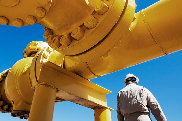 oil refinery worker standing next to yellow pipeline
